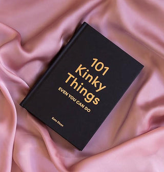 A copy of 101 Kinky Things Even You Can Do with black cover and gold lettering rests on a rippled piece of pink satin