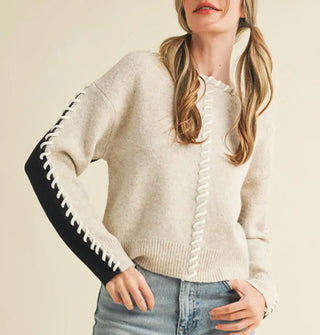 Model wears a cream-colored sweater with black arm panel and whip stitching down the arm, front center, and neckline