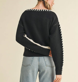Model wears a black-backed sweater with white arm panel and white whip stitching along the neckline and down the sides of the arms