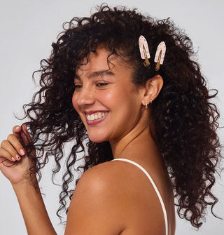 Smiling model wears two hair clips in a side-swept curly style
