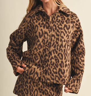 Model touches the bottom hem of a leopard print jacket with an oversized fit and matching cloth-covered buttons, paired with matching skirt
