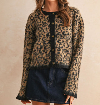 Model wears a leopard print button-down cardigan with black placket, neckline, and sleeve cuffs paired with a dark wash denim skirt