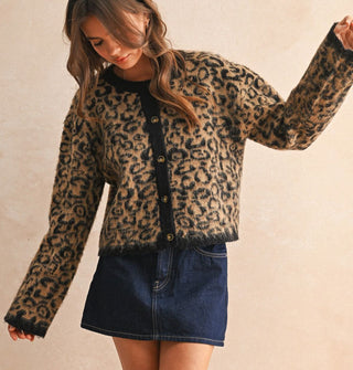 Model with arms outstretched wears a leopard print button-down cardigan with black placket, neckline, and sleeve cuffs paired with a dark wash denim skirt
