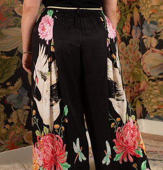 Model with back to camera wears ultra wide-legged black pants with large print of flowers and cranes