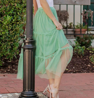 Model wears a seafoam green tulle midi-length skirt with knee-length lining and three horizontal tiers edged with ruffles