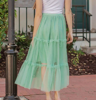 Model wears a seafoam green tulle midi-length skirt with knee-length lining and three horizontal tiers edged with ruffles
