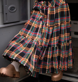 Model stepping out of a camping trailer and kicking out one leg wears a multicolored plaid ruffle-tier skirt
