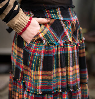 Closeup of model's hand in the pocket of a black ruffle-tier skirt with colorful plaid print
