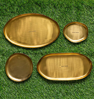 Four gold-toned platters with shallow rims, all different sizes and dimensions and stamped with the words, "Rosy Rings," are placed on green astroturf