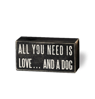 Rectangular black box sign with distressed finish says, "All you need is love... and a dog" in large white lettering