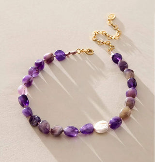 Necklace with gold clasp and extender chain is strung with polished purple amethyst stones and one accent pearl