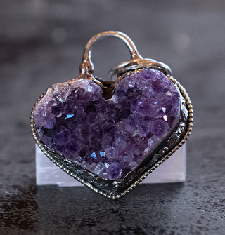 Heart-shaped pendant with purple amethyst cluster center inside an ornate silver setting with top arc bail and rings