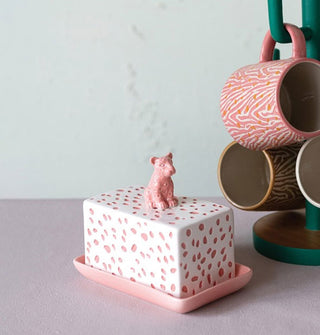 Pink and white spotted leopard ceramic butter dish on a countertop next to a mug tree