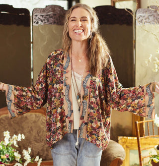 Smiling model wears a floral-patterned silken jacket top with script banner detail on the trim