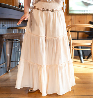 Model wears light peachy-pink, wide-legged pants with horizontal ruffled tiers