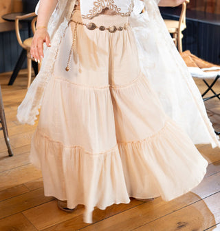 Model wears light peachy-pink, wide-legged pants with horizontal ruffled tiers