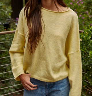 Model wears a slouchy yellow sweater with rolled boat neckline