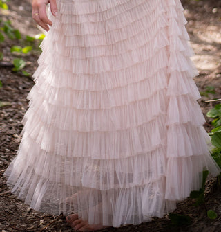 Model wears a multi-tiered ruffled light pink tulle maxi skirt in a forest setting