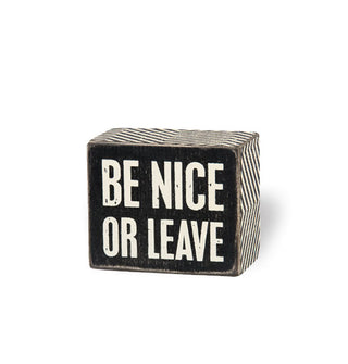 Black-faced distressed wood sign says, "Be nice or leave" in large white lettering and features a black and white zigzag-patterned edge