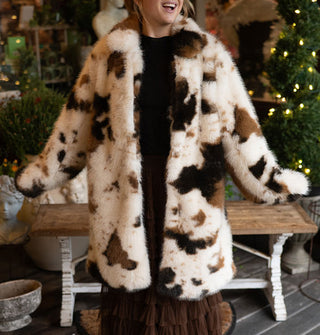 Smiling model with arms outstretched wears a white and brown cowhide print faux fur coat