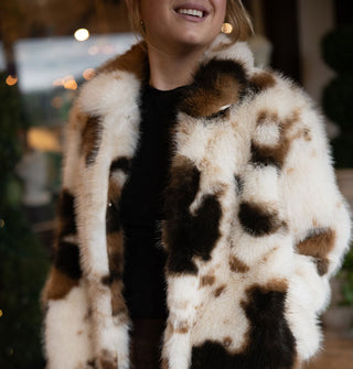 Smiling model wears a white and brown cowhide print faux fur coat