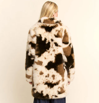 Model facing away from the camera wears a white and brown cowhide print faux fur coat