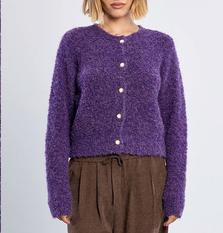 Model wears a purple bouclé knit cardigan with white pearlescent buttons