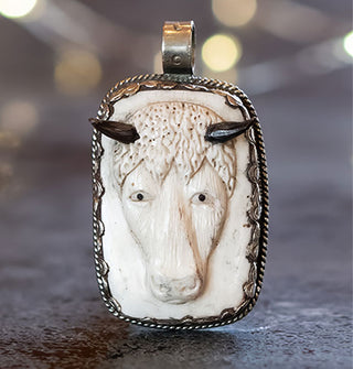 Rectangular white carved bone pendant depicting a bison's head with black agate horns in a silver pendant setting with rounded top bail