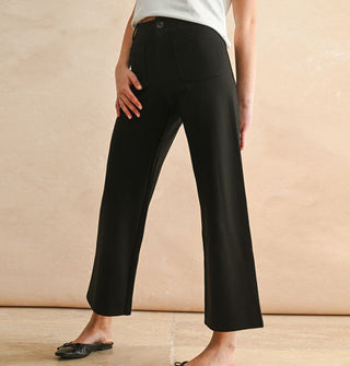 Model wears a pair of cropped flared black pants with pockets, belt loops, and button closure with a pair of ballet slip-ons