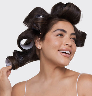 Smiling model pulls a black roller from hair while others are held in place at sides and top of head