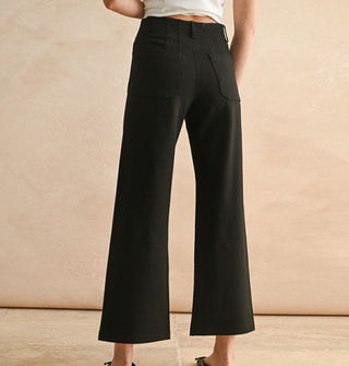 Model wears a pair of cropped flared black pants with pockets and belt loops