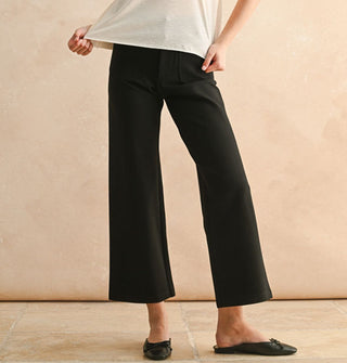 Model wears a pair of cropped flared black pants with ballet flat slip-ons
