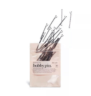Black bobby pins appear to fly upward out of light pink Kitsch packaging