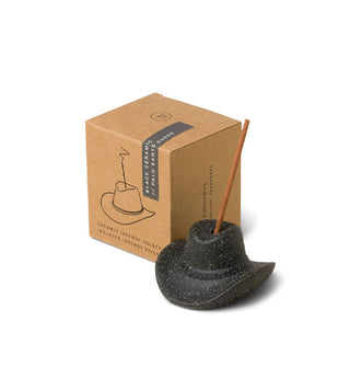 Black ceramic cowboy hat incense holder fitted with an incense stick next to its brown gift box packaging
