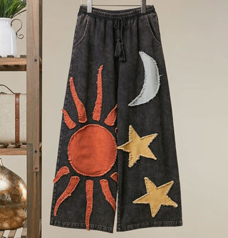 Black tie waist wide-legged pants with orange sun, gray moon, and yellow stars appliqués, all with rough edges