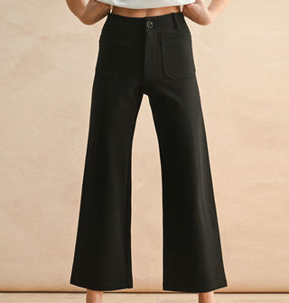 Model wears a pair of cropped flared black pants with pockets, belt loops, and button closure