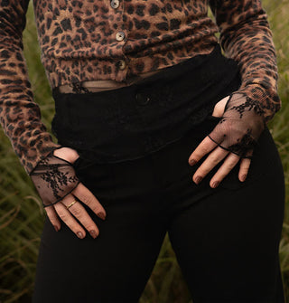Model hooks thumbs in the pockets of black pants worn with a long-sleeved leopard print cardigan and fingerless black lace gloves