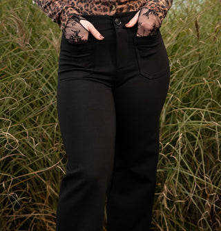 Model stands with hands in the pockets of black pants worn with a long-sleeved leopard print cardigan and fingerless black lace gloves