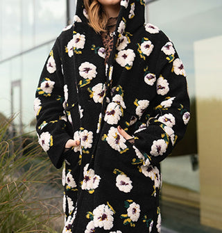 Model wears a black hooded coat with plush white floral pattern in front of a glass structure