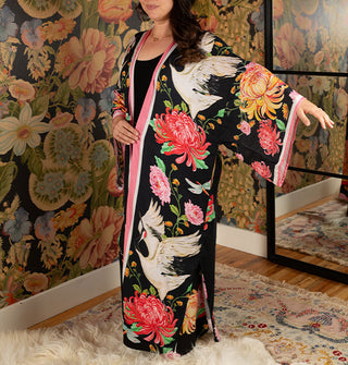 Model wears a long black robe with bold floral and cranes print and contrast stripe edging