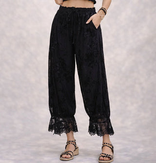 Model wears black pantaloons with flocked velvet floral pattern, elasticated tie waist, and lace trim