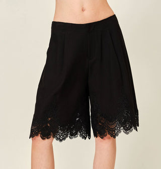 Model wears black wide-legged, knee-length shorts with lace hem detail