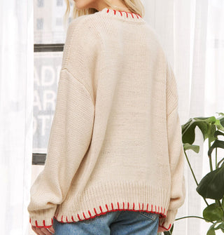 Model wears an oversized cream-colored sweater with red blanket stitching on the neck, sleeve, and bottom hems