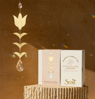 A gold and crystal flower and leaves suncatcher throws rainbows against the wall and accompanying gift box behind it