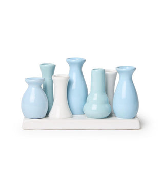 Series of small porcelain bud-sized vases in blues and whites are clustered together on a white rectangular base