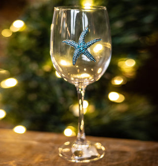 Twinkling tree lights shine through a clear wine glass with a blue rhinestone-encrusted starfish decal on its bowl