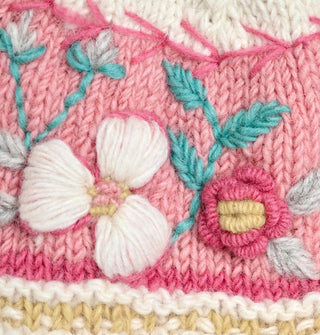 Closeup of knit floral embroidery in light pink, dark pink, gray, white, aqua, and light yellow