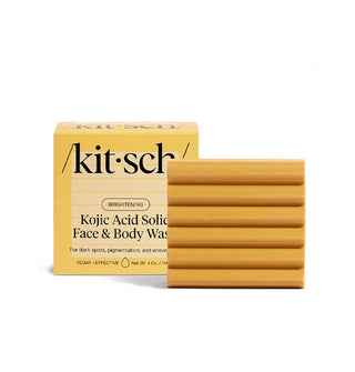 Gold square ribbed bar of Kitsch Brightening Kojic Acid Solid Face & Body Wash sits next to and slightly in front of its box packaging