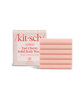 Pink square ridged bar of Kitsch Cleansing Tart Cherry Solid Body Wash sits alongside and slightly in front of its box packaging