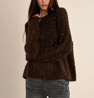 Model wears a slouchy brown sweater with multicolored fabric flecks and small sequins sewn in